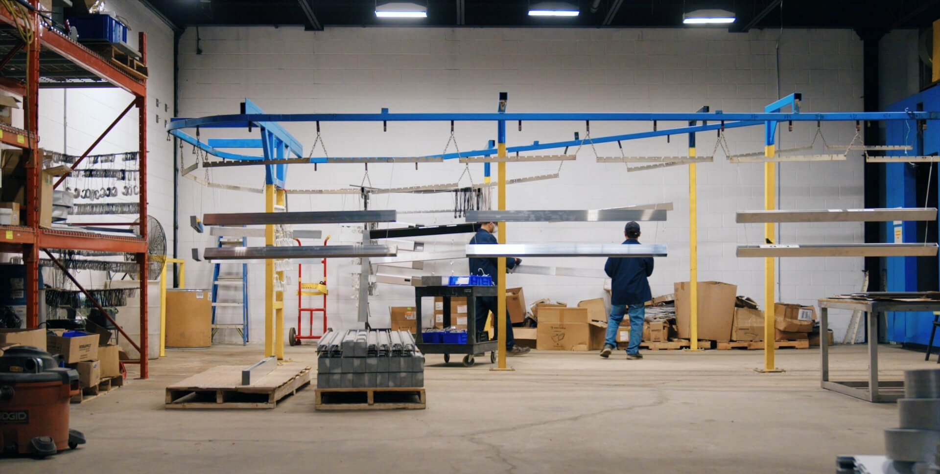 workers hanging metal parts before they enter a paint booth